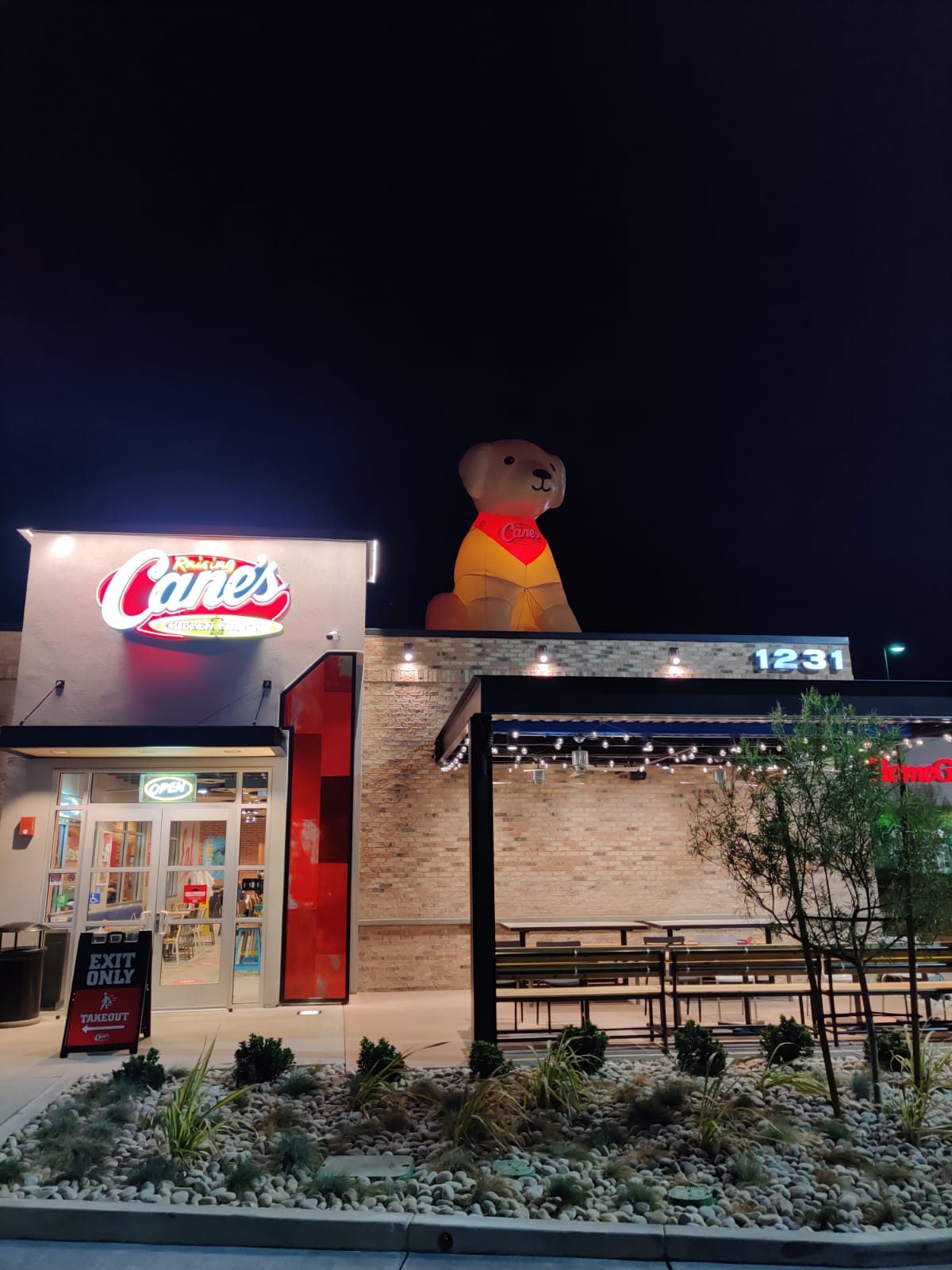 Inflatable Raising Cane's dog mascot lit from inside on a restaurant rooftop at night