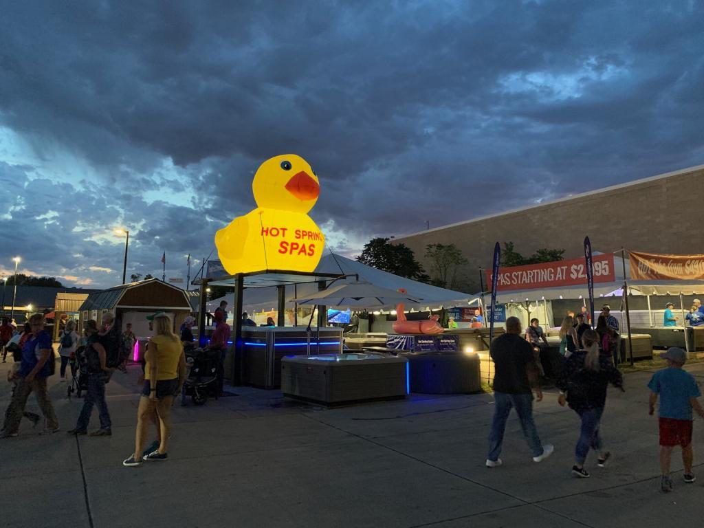Inflatable yellow duck lit from inside above a hot tub display at a night fair